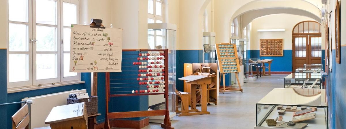 Schulbänke, Vitrinen und Objekte im Flur, links Fensterfront zum Schulhof. Schulbänke, Vitrinen und Objekte im Flur, links Fensterfront zum Schulhof.
