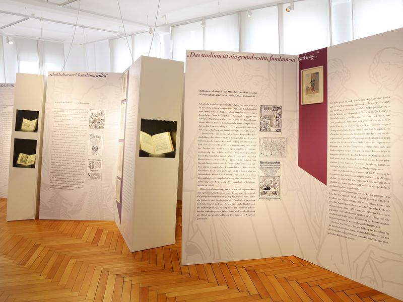 Erster Raum mit den in Buchform gestalteten Texttafeln und Objekt-Vitrinen. Link zur Unterseite "Dauerausstellung".