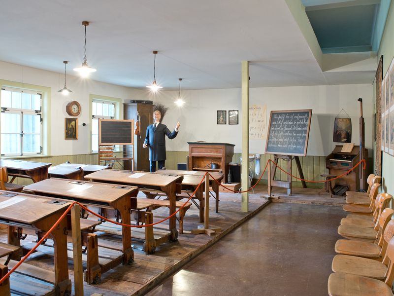 Das Historische Klassenzimmer mit Schülerpulten und Lehrerpuppe. Link zur Unterseite "Führungen für Schulklassen".